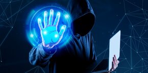 Zakapturzona postać trzyma laptop i wyciąga w stronę ekranu niebieską dłoń 