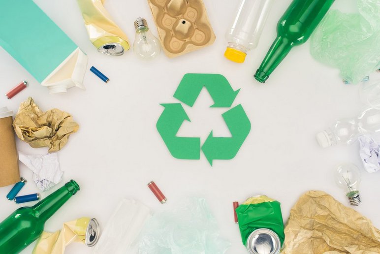Widok z góry na śmieci różnego rodzaju leżące wokół zielonego znaku recyklingu. Stock images by Depositphotos