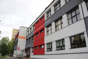 Budynek Centrum Kształcenia Zawodowego i Ustawicznego w Żorach – nowoczesna, odnowiona elewacja w kolorach szarym, czerwonym i białym, z dużymi oknami i szyldem „CKZiU Żory” oraz napisem „Centrum Kształcenia Zawodowego i Ustawicznego w Żorach” nad wejściem. Po lewej stronie widoczne drzewa i fragment osiedlowego bloku.