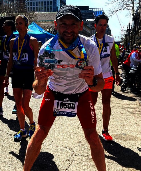 Grzegorz Pysz na mecie Maratonu Bostońskiego trzyma w dłoniach dwa medale. 